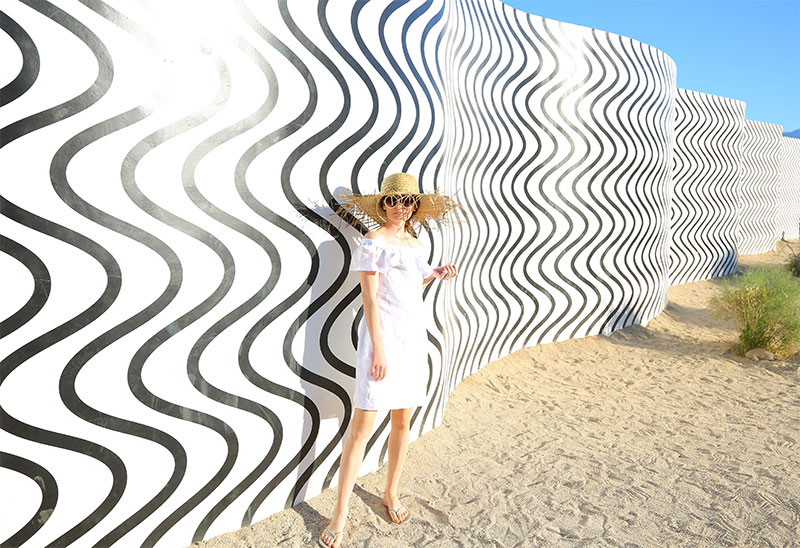Cute White Dresses for Summer: Fashion blogger Kelly Golightly visits Desert X in Palm Springs wearing a Sail to Sable LWD + Lack of Color straw hat. #kellygolightly #desertx #lwd #lackofcolor #murals #littlewhitedress