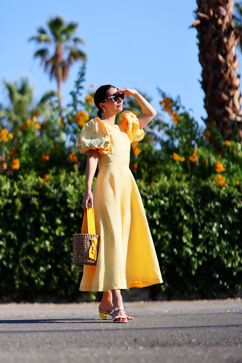 Top fashion blogger Kelly Golightly wears a Fanm Mon Yellow Dress in front of orange flowers in Palm Springs.