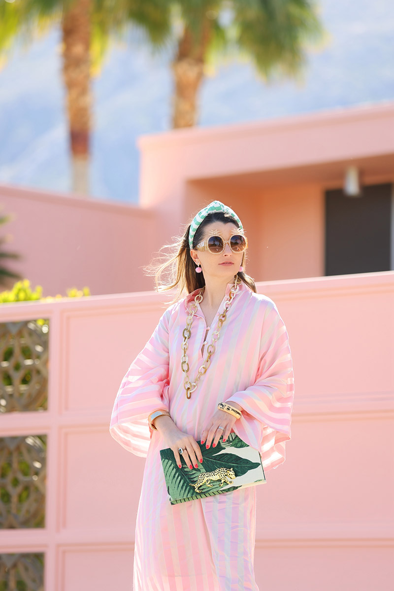 Kelly Golightly wears a pink and white striped La Vie caftan for less in front of a pink house in Palm Springs.